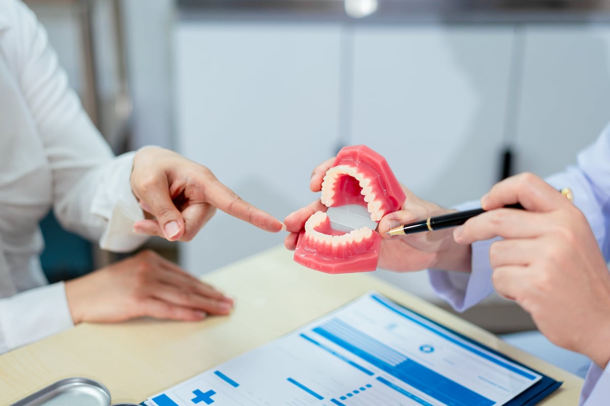 Dentista explicando un tratamiento a una paciente con un modelo dental en la consulta